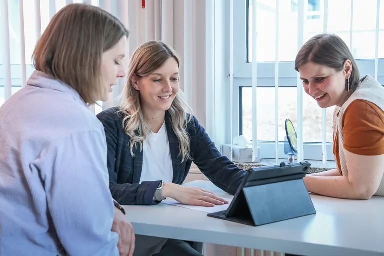 Drei Kolleginnen der Praxis Fischer schauen gemeinsam lächelnd auf ein Tablet