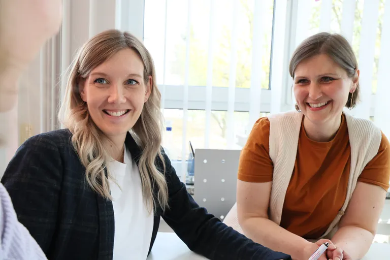 Zwei Kolleginnen der Praxis Fischer lachen gemeinsam in einer Besprechung
